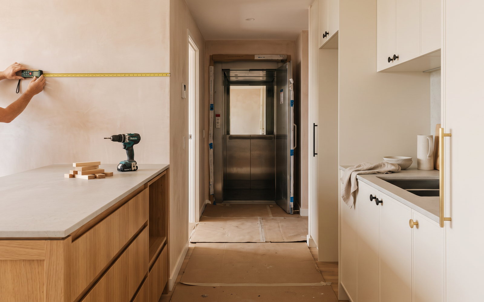 Joiner measuring apartment kitchen walls beside a protected service lift